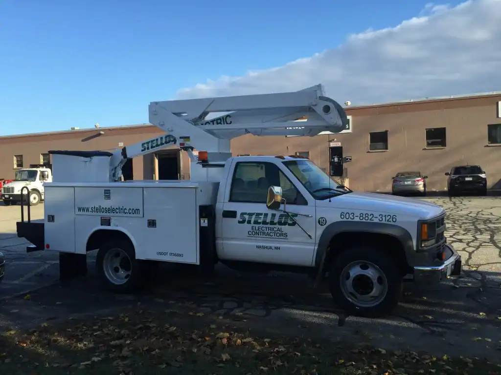 A white utility truck with a raised bucket lift, used by New Hampshire electrical contractors, is parked outside.