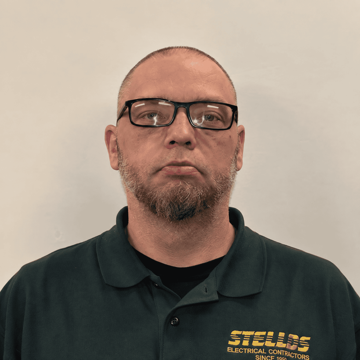 A man wears glasses and a green Stellos Electrical Contractors polo shirt.